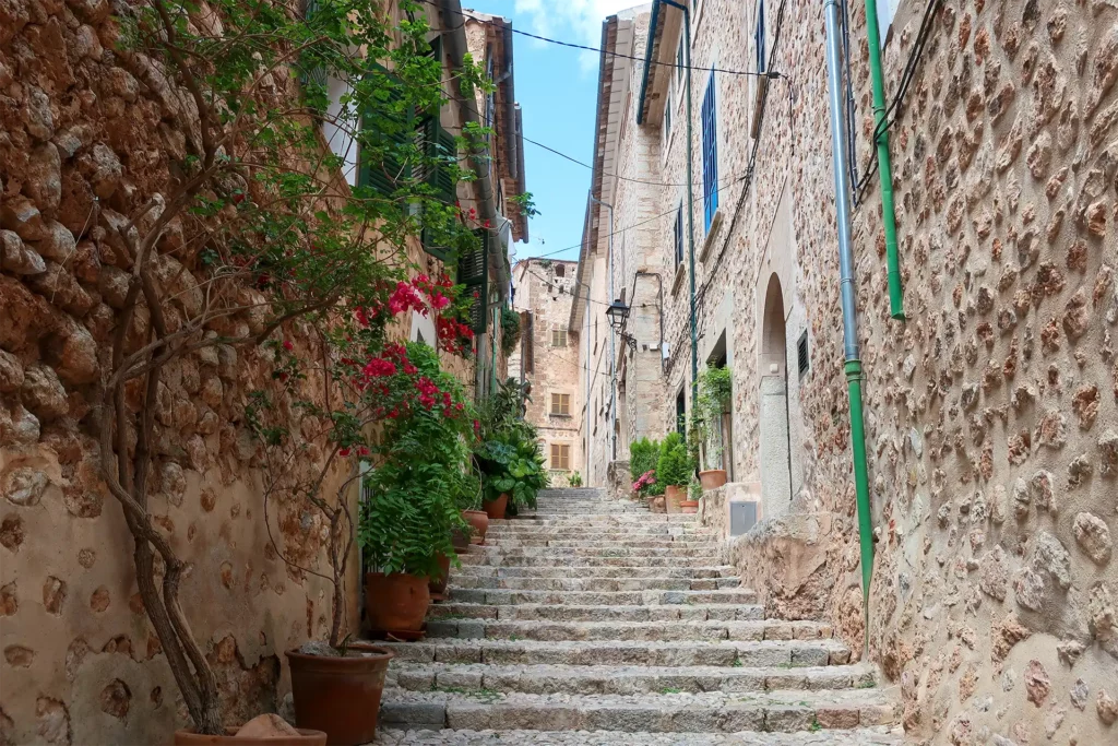 Idyllic village of Fornalutx, Mallorca: Narrow streets lined with traditional stone houses, adorned with colourful flowers and surrounded by lush green mountains.