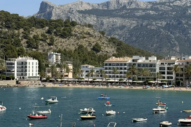 View of Port de Soller beach on a sunny summer day, with clear blue skies and a stunning mountain backdrop
